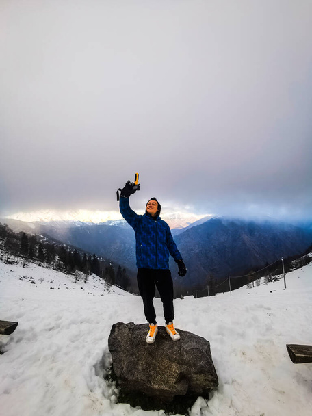  young boy taking selfie footage with action cam of him standing and smiling with great mountain view in background. Concept of modern lifestyle and social media travel content sharing - Foto, imagen
