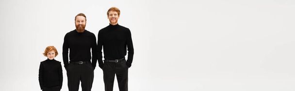 red haired and bearded men in black clothes standing with hands in pockets near happy boy isolated on grey, banner - Fotoğraf, Görsel