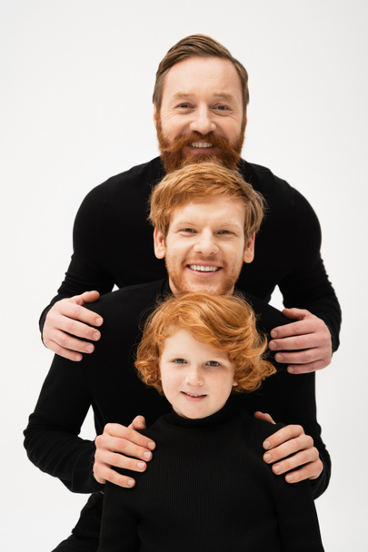 happy men in black sweaters smiling at camera near redhead boy while posing isolated on grey - Zdjęcie, obraz