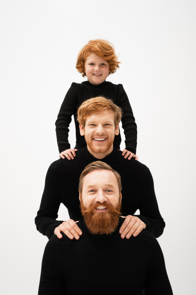 happy redhead boy and bearded men in black turtlenecks looking at camera while posing isolated on grey - Foto, Imagem