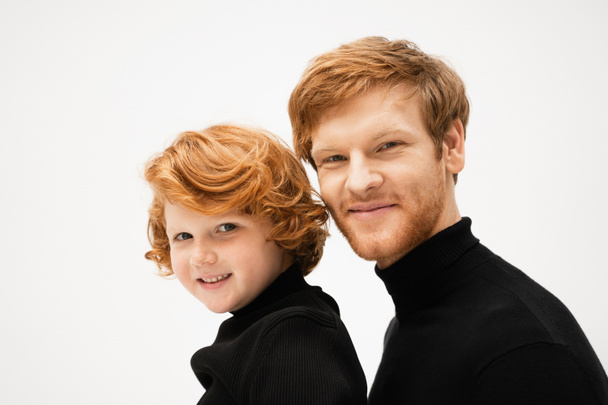 family portrait of redhead dad and son in black sweaters smiling at camera isolated on grey - Foto, Imagen