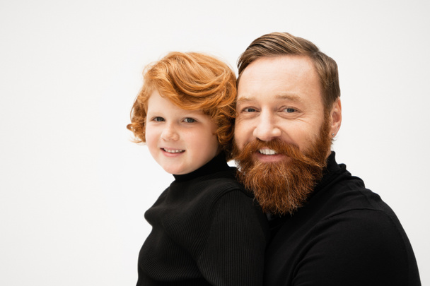 joyful bearded man with redhead grandson smiling at camera isolated on grey - Photo, image