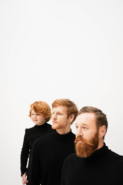 redhead men and happy kid in black pullovers looking away isolated on grey with copy space - Zdjęcie, obraz