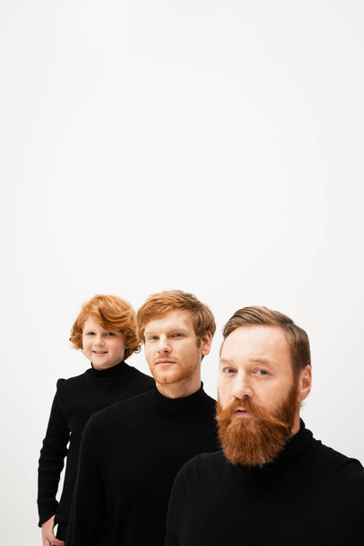 bearded man looking at camera near redhead son and smiling grandson in black turtlenecks isolated on grey - Foto, imagen