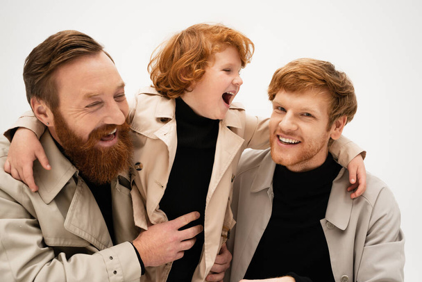 excited boy laughing and embracing father and bearded grandpa isolated on grey - Foto, imagen
