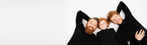 top view of cheerful bearded man with red haired son and grandson smiling at camera while lying on light grey background, banner - Foto, Bild