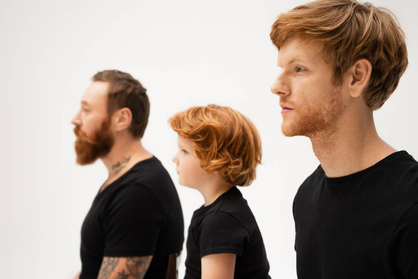 side view of redhead boy near dad and bearded grandfather in black t-shirts isolated on grey - Foto, Bild