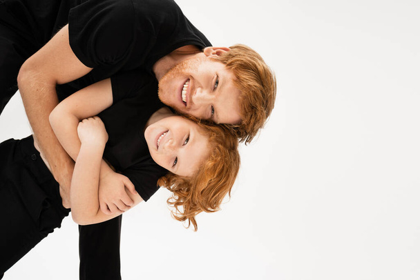 happy man embracing redhead son while having fun and looking at camera isolated on grey - Foto, imagen