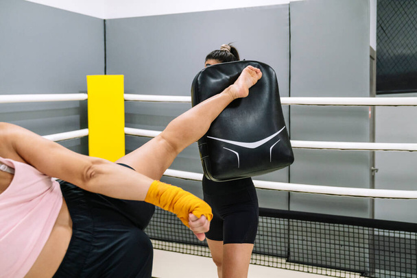 Неузнаваемая женщина-кикбоксер дает высокий удар в тренировке со своим тренером на ринге. - Фото, изображение
