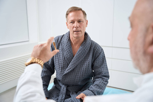 Muž středního věku komunikuje s lékařem v lékařském středisku, dostává konzultaci o plazmové terapii - Fotografie, Obrázek
