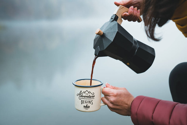 Young woman hiker pouring fresh coffee into cup or mug from moka pot coffee maker outdoor. - Zdjęcie, obraz