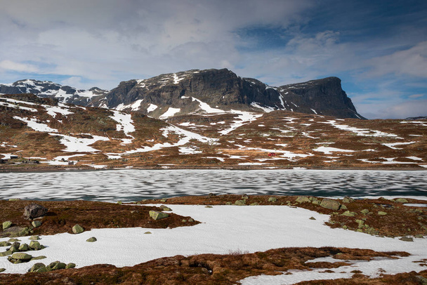Snowy landscape of Hardangervidda with mountains and icy lake in Norway, red hut at the lakeside - Fotó, kép