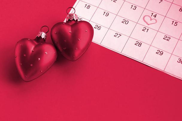 Dvě červená srdce a kalendář označené 14. února, koncept Valentýna, výročí. Obraz tónovaný ve Viva Magenta, barva roku 2023. - Fotografie, Obrázek