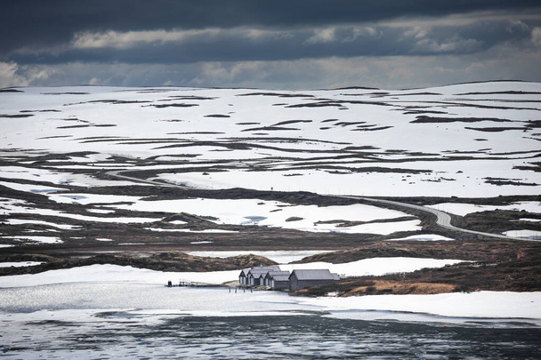 Каюты на набережной замёрзшего озера в ландшафте Национального парка Хардангервидда в Норвегии, снег и лед на земле - Фото, изображение