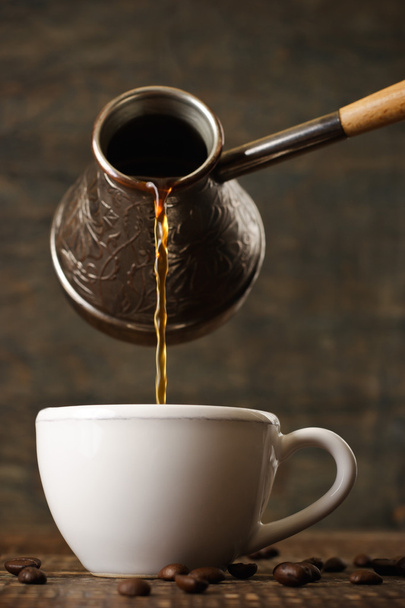 Café oscuro vierte de un jezve de cobre en una taza blanca
 - Foto, imagen