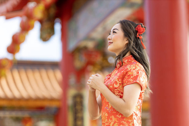 Азиатская женщина в красном платье Чхонсам Кипао загадывает желание богу предков в китайском буддийском храме во время лунного Нового года для благословения и удачи - Фото, изображение