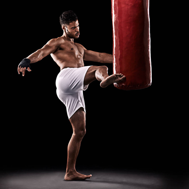 Give it all youve got. Studio shot of kick boxer working out with a punching bag against a black background - Foto, Bild
