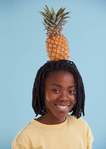 Lets get tropical. A cropped view of a young african teen with a pineapple on his head in the studio - Foto, Imagen