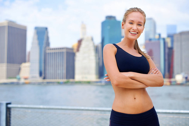 Fitness im Großstadtdschungel. Porträt einer schönen jungen Frau, die neben einem Fluss steht, während sie in der Stadt auf der Flucht ist - Foto, Bild