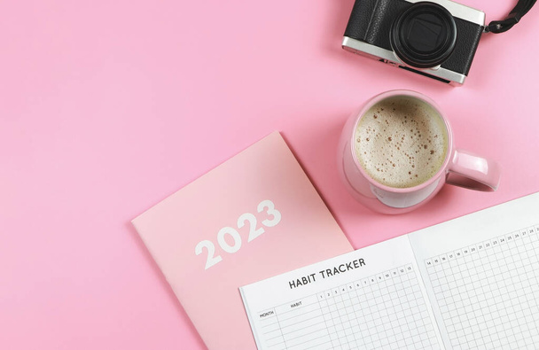 Top näkymä tai tasainen lay tapana tracker kirja vaaleanpunainen päiväkirja tai suunnittelija 2023, vaaleanpunainen kuppi kahvia ja digitaalikamera vaaleanpunainen tausta kopioi tilaa. - Valokuva, kuva