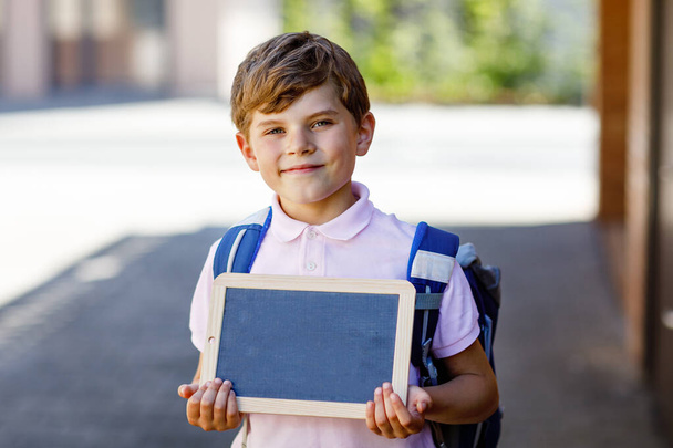 Happy little kid boy with backpack or satchel. Schoolkid on the way to school. Healthy adorable child outdoors On desk Last day second grade in German. Schools out. - Photo, Image