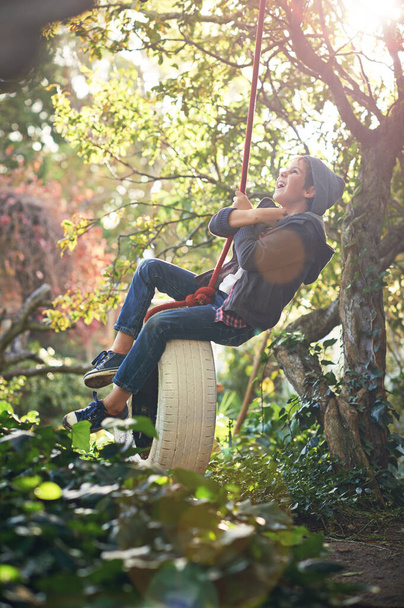 Μην ξεχάσεις να παίξεις. Ένα έφηβο αγόρι αιωρείται σε μια κούνια ελαστικών στον κήπο - Φωτογραφία, εικόνα