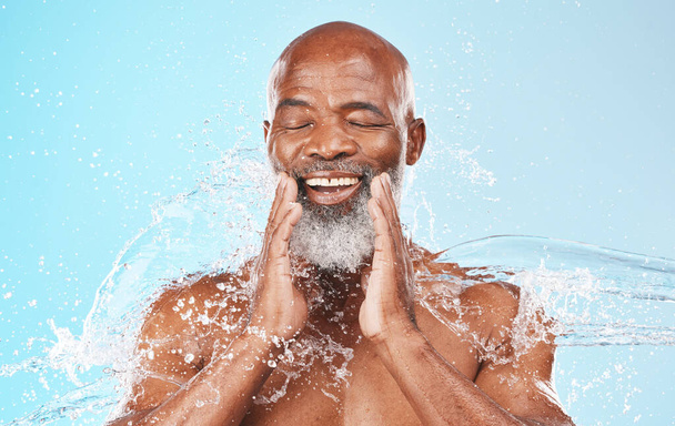 健康、化粧品やシャワーのための青の背景に幸せな黒人の顔、水と掃除。スタジオ男性モデル、笑顔と顔の健康のためのバスルームでの水スプラッシュ、審美的なスキンケアとスパ. - 写真・画像