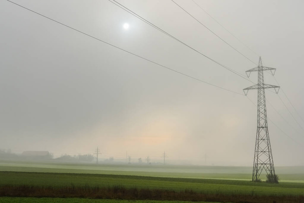 ένας στύλος ισχύος με πυκνή ομίχλη και ήλιο στον ουρανό το χειμώνα - Φωτογραφία, εικόνα