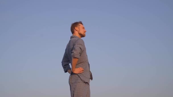 Cheerful bearded caucasian male in nightwear making morning exercises with positive emotion. Clear blue sky at background. Outdoor workout or physical activity concept. High quality 4k video footage - Imágenes, Vídeo