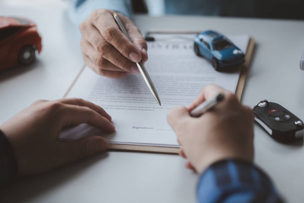 A car rental company employee pointed out the renter to sign the rental agreement after discussing the details and rental terms with the renter. Concept of car rental. - Foto, Imagem