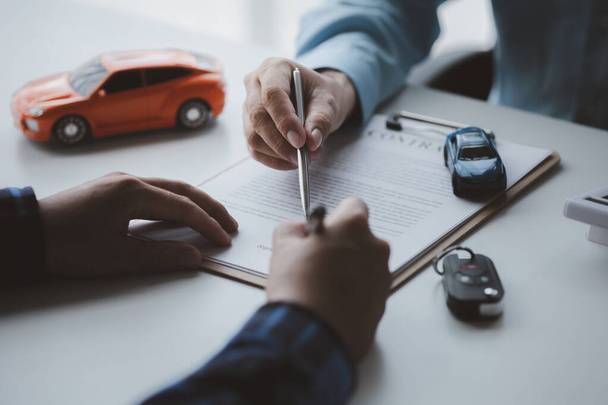Egy autókölcsönző cég alkalmazottja rámutatott a bérlőre, hogy írja alá a bérleti szerződést, miután megbeszélte a részleteket és a bérleti feltételeket a bérlővel. Az autókölcsönzés fogalma. - Fotó, kép