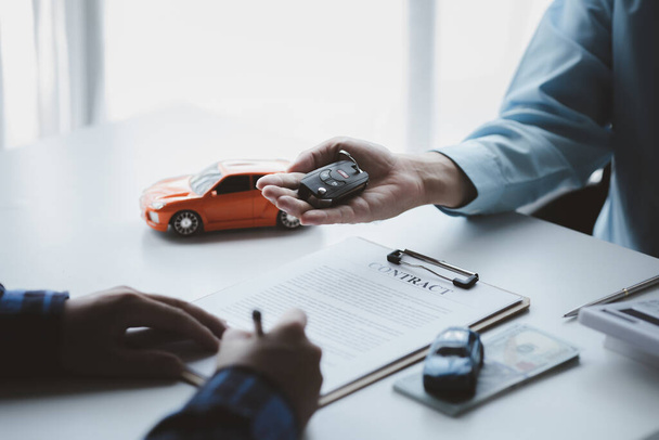 Egy autókölcsönző cég alkalmazottja rámutatott a bérlőre, hogy írja alá a bérleti szerződést, miután megbeszélte a részleteket és a bérleti feltételeket a bérlővel. Az autókölcsönzés fogalma. - Fotó, kép