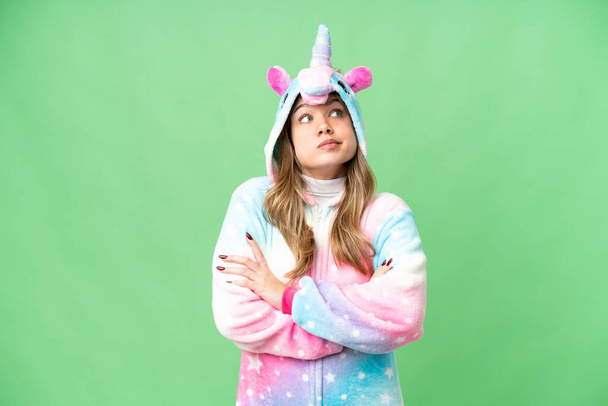Chica joven con pijama de unicornio sobre fondo de croma clave aislado haciendo gestos de dudas mientras levanta los hombros - Foto, imagen