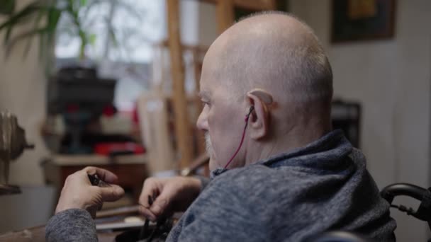 Oudere meesterjuwelier in rolstoel werkt in een werkplaats met een bankschroef - Video