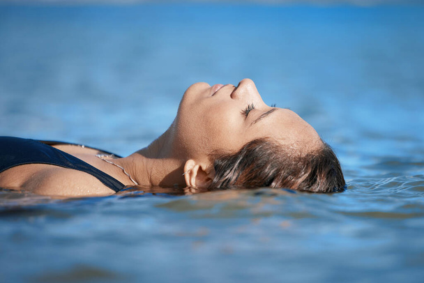 Woman swimming, travel or fitness in ocean with peace, calm and exercise, wellness and waves at beach. Relax, female swimmer floating and sea with nature, freedom and water sport on summer vacation. - Foto, Imagem