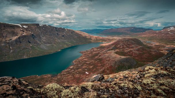 Blue lake in mountain landscape from above the hike to Knutshoe summit in Jotunheimen National Park in Norway, mountains of Besseggen in background, cloudy sky, moss in the foreground - Foto, Imagem