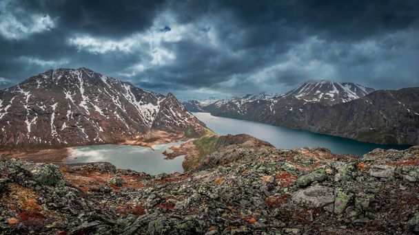 Turquoise and blue lakes in mountain landscape from above the hike to Knutshoe summit in Jotunheimen National Park in Norway, mountains of Besseggen in background, dramatic cloudy sky with rain - Photo, Image