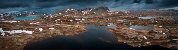 Panorama landscape with blue lakes, mountains and road of Jotunheimen National Park in Norway from above, dramatic dark cloudy sky - Foto, Imagem
