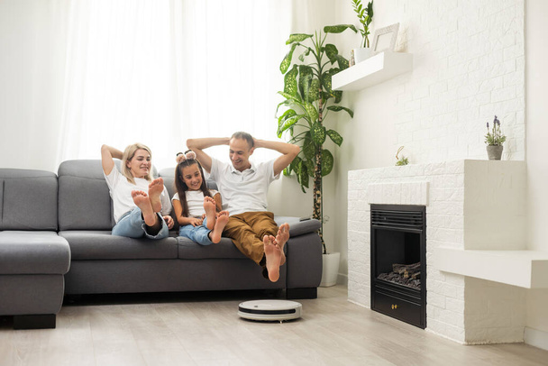 Улыбающаяся семья указывает на роботизированный пылесос. - Фото, изображение