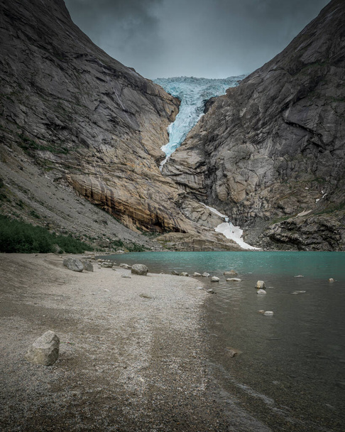 ノルウェーのJostedalbreen国立公園の山の中でBriksdalbreen氷河の氷,ターコイズブルーの氷河湖,ビーチ沿いの岩 - 写真・画像