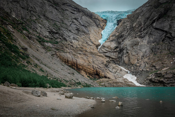 Briksdalsbreen glacier ice in the mountains of Jostedalsbreen national park in Norway, turquoise glacier lake, rocks along the beach - Photo, image