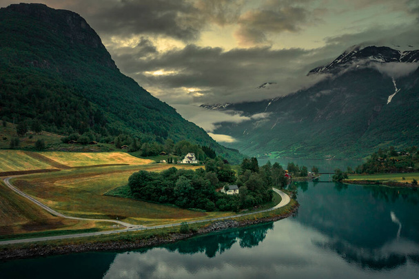 Aerial view of road in landscape of fjord at Briksdalsbreen glacier in Jostedalsbreen mountains during summer sunset, clouds in blue sky - Photo, image