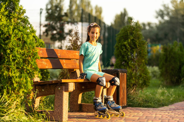 little girl wears roller skates on beautiful summer day in a park. - 写真・画像