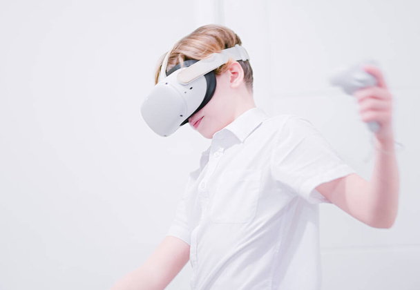 Νεαρό έφηβο αγόρι που φοράει κεφάλι εικονικής πραγματικότητας σε καθαρό λευκό εσωτερικό. - Φωτογραφία, εικόνα