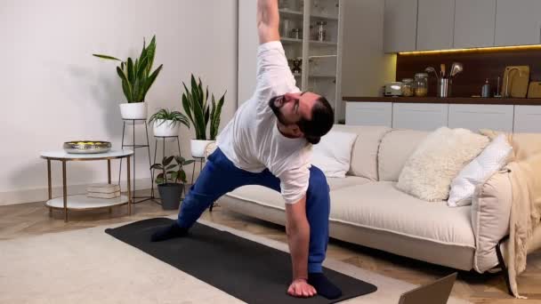 Sporty man having workout at home watching online training classes by using laptop. Mid adult man doing worlds greatest stretch exercise following video tutorial on computer indoors. Daily Exercising - Filmmaterial, Video