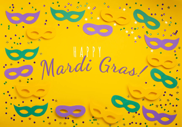 Mardi Gras gold color beads with Masquerade festival carnival masks and golden, green, purple confetti on yellow background. Party invitation, greeting card, venetian carnivale celebration concept. - Photo, Image