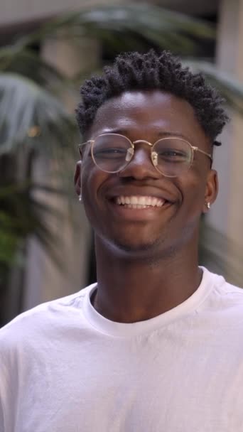 Ritratto di uomo nero molto felice, sorridente e guardando la macchina fotografica. Uno studente afroamericano sorride sinceramente stando all'aperto. Il tipo indossa una maglietta bianca. - Filmati, video
