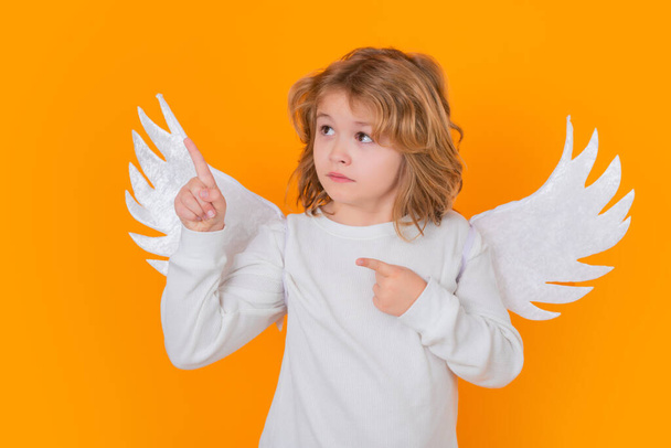 Child angel pointing finger, point gesture. Valentines day banner. Cute child with angel wings. Studio portrait of angel child on studio color isolated background with copy space - Foto, immagini