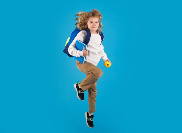 Kid jump and enjoy school. School child in school uniform with bagpack and globe jump. School children jumping on studio isolated blue background - Photo, image