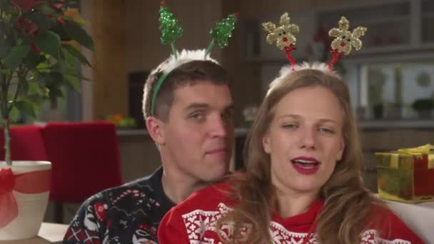 Portrait:クリスマスのイブでお祝いの気分の歌とダンスで楽しいカップル。クリスマスのセーターで陽気な二人組休日を祝い、快適なソファでリラックスしたお祝いの時間を楽しむ. - 映像、動画